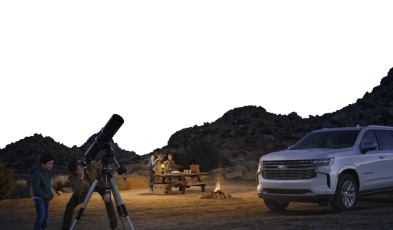 A Chevrolet sitting in a desert while a family camps out nearby.